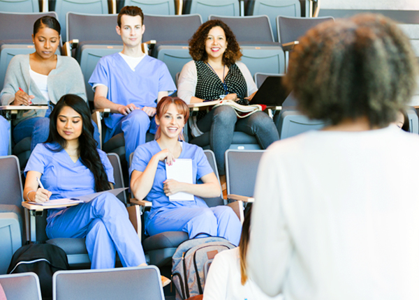 College students dressed in scrubs attend a lecture, embodying the idea of community college insurance. 